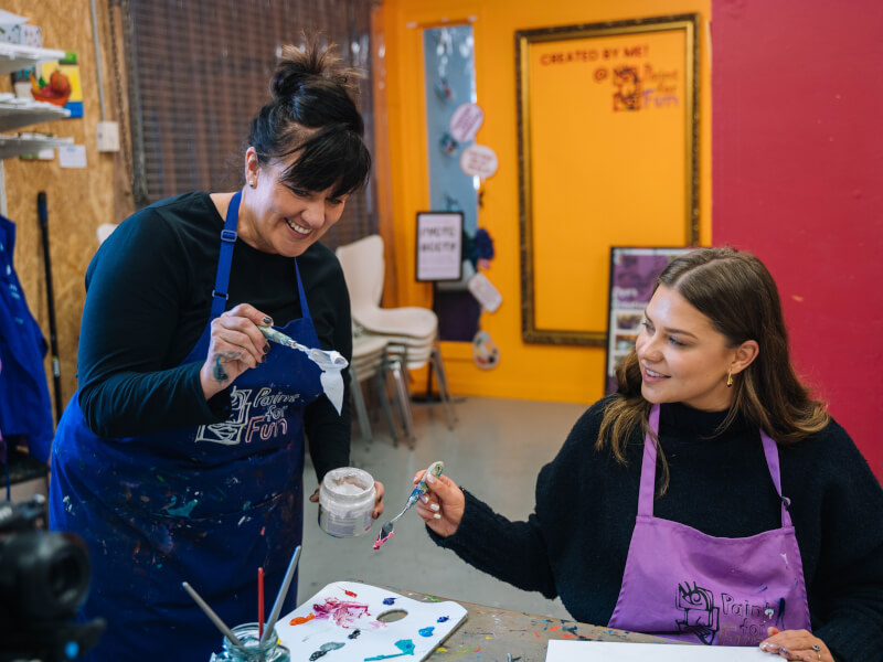 Two women smiling and loading an artist's palette with acrylic paints